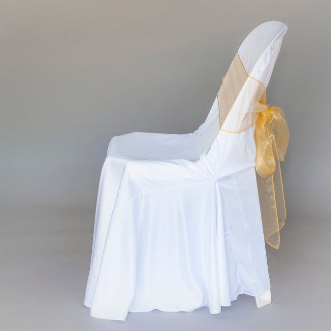 White chair with sheer fabric and gold ribbon on a plain gray background