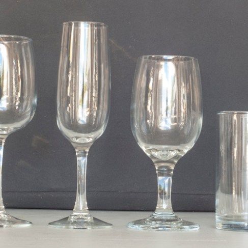 Assorted clear drinking glasses and champagne flutes arranged on a table against a dark background