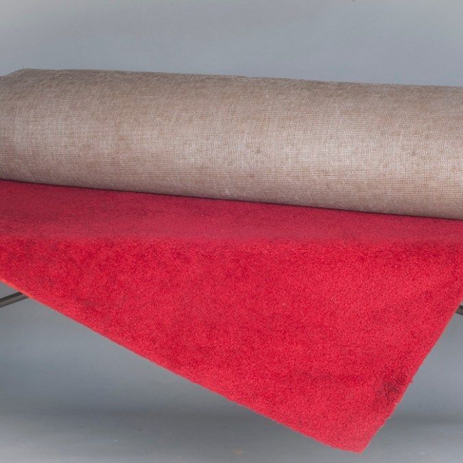 Folded red and beige carpet rugs stacked on a gray surface
