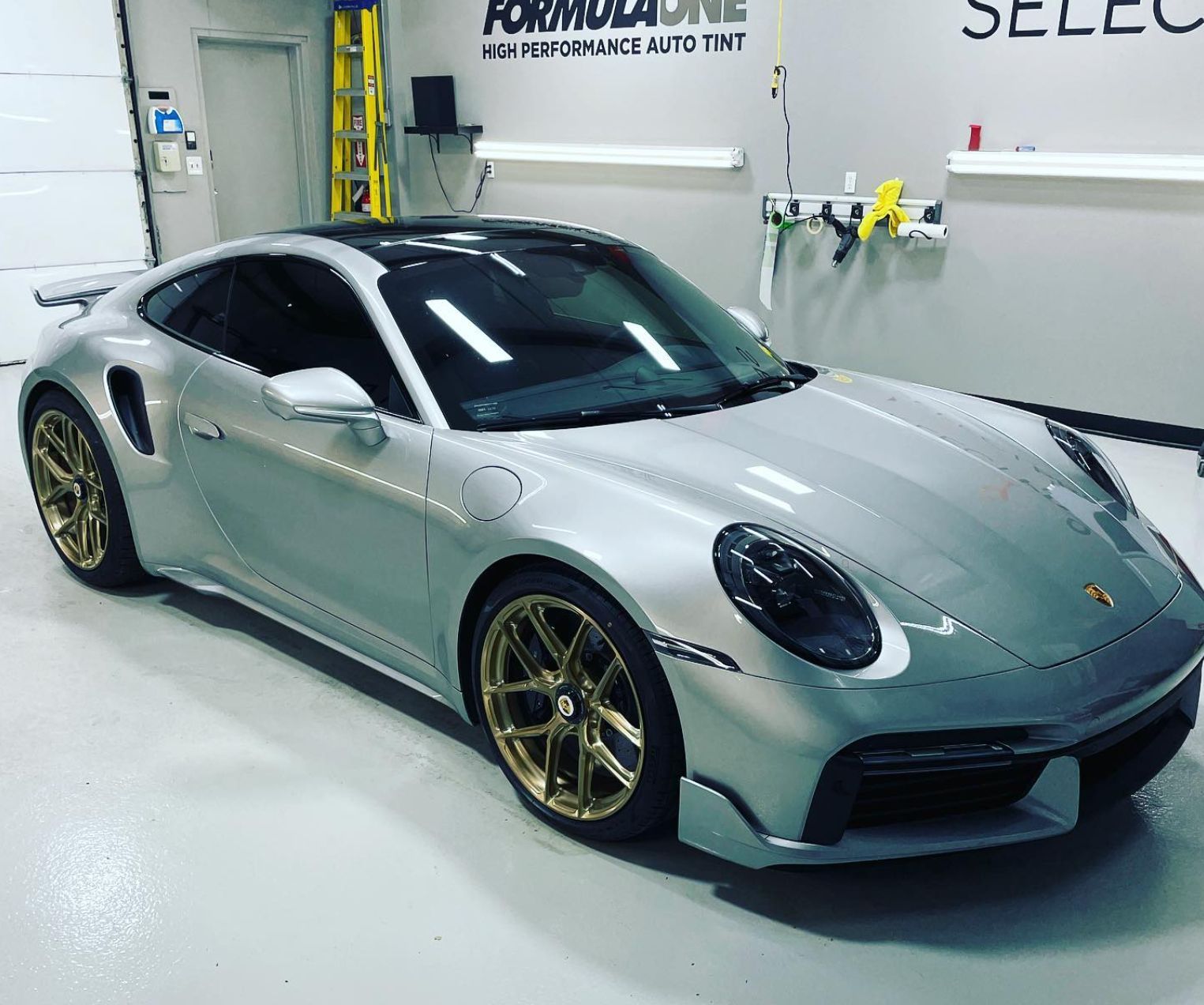Silver Porsche 911 Turbo S with gold wheels in an auto tint shop.