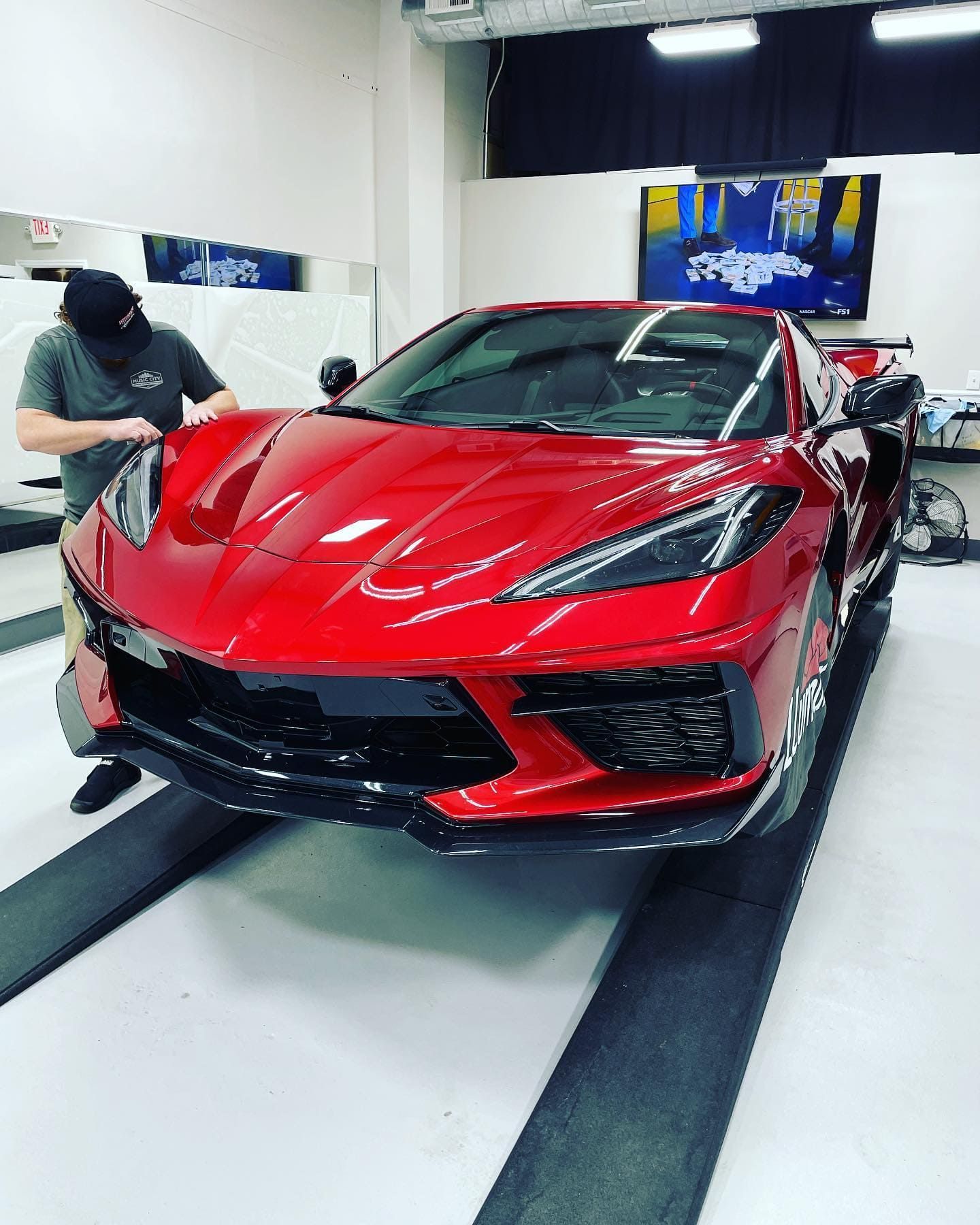 Worker applying protective film to a metallic red Chevrolet Corvette C8.