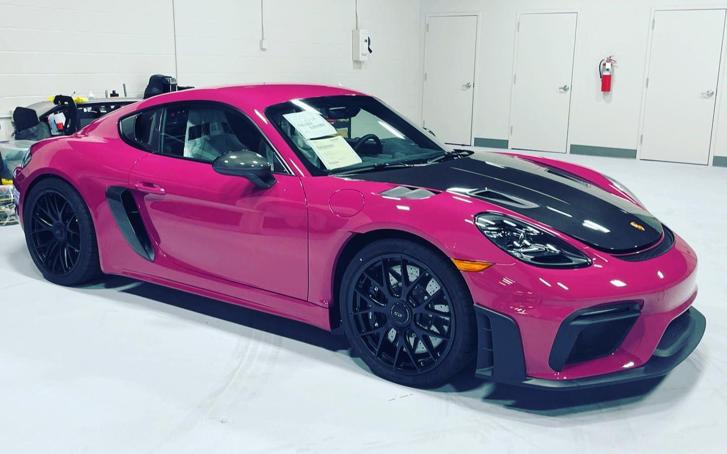 Bright pink Porsche 718 Cayman GT4 RS with a black hood parked indoors.