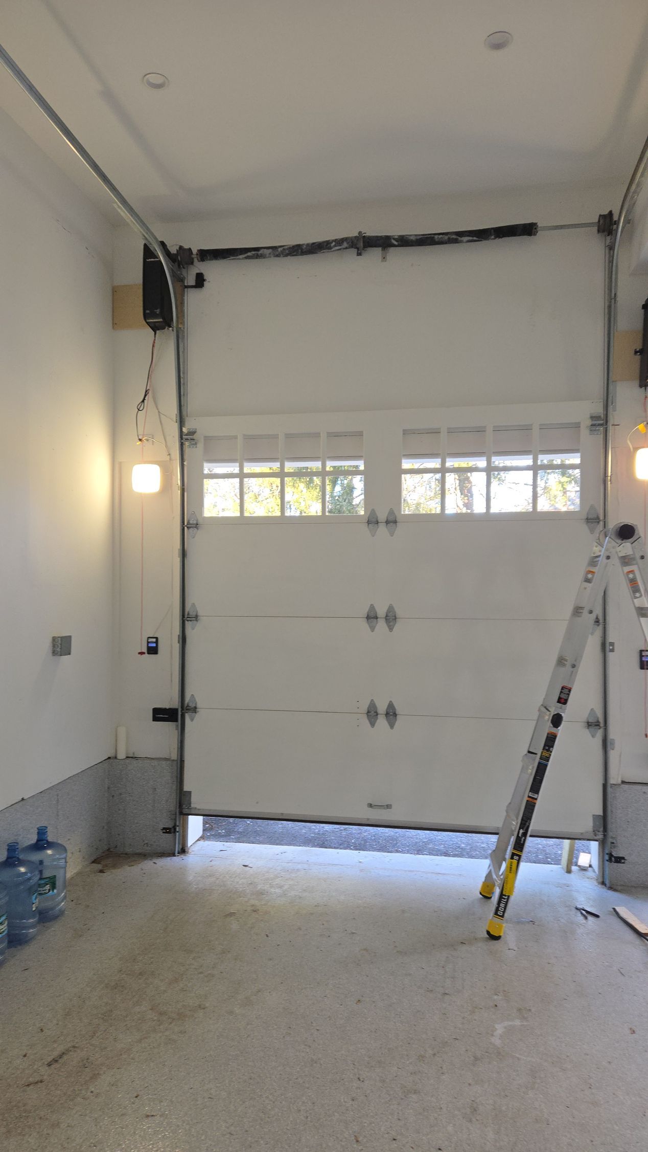 White closed garage door inside a garage. A ladder leans against the right side.