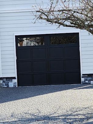 A black garage door is sitting in front of a white house.