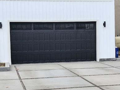 A black garage door is sitting in front of a white house.