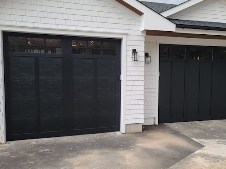 Two black garage doors are on a white house.