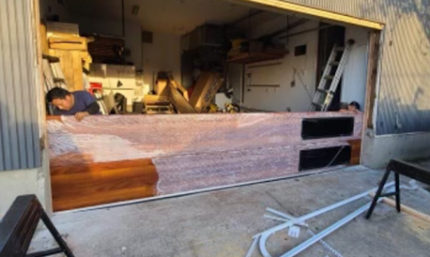 A man is working on a large piece of wood in a garage.