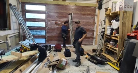 Two men are standing in a garage looking at a garage door.