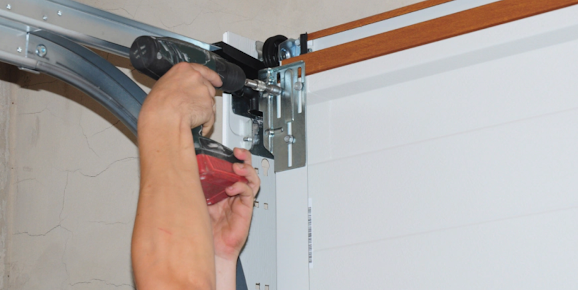 A person is fixing a garage door with a drill.