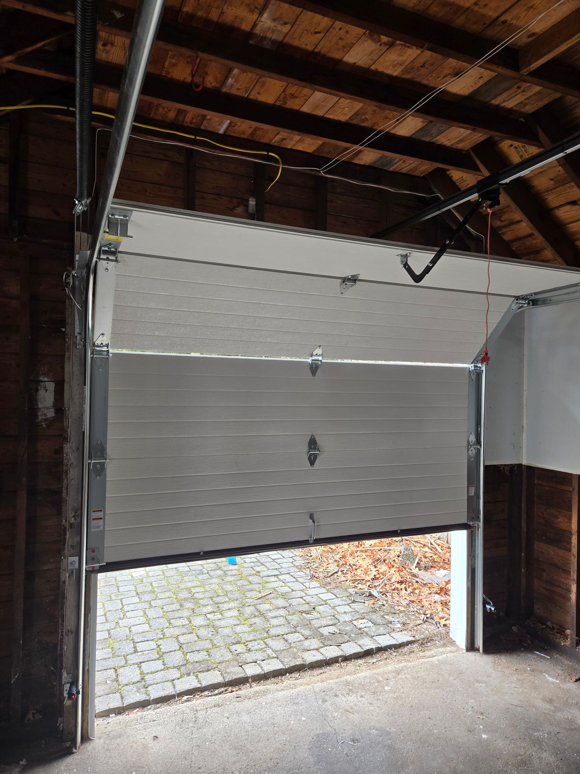 Garage door partially open, revealing a brick pathway. The door is white and the interior has exposed wood.
