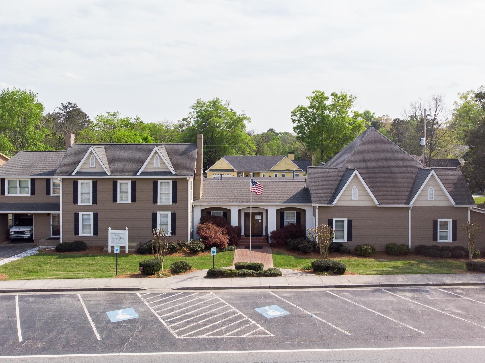Apartment and office building with U.S. flag, parking spaces, and landscaped front under overcast sky