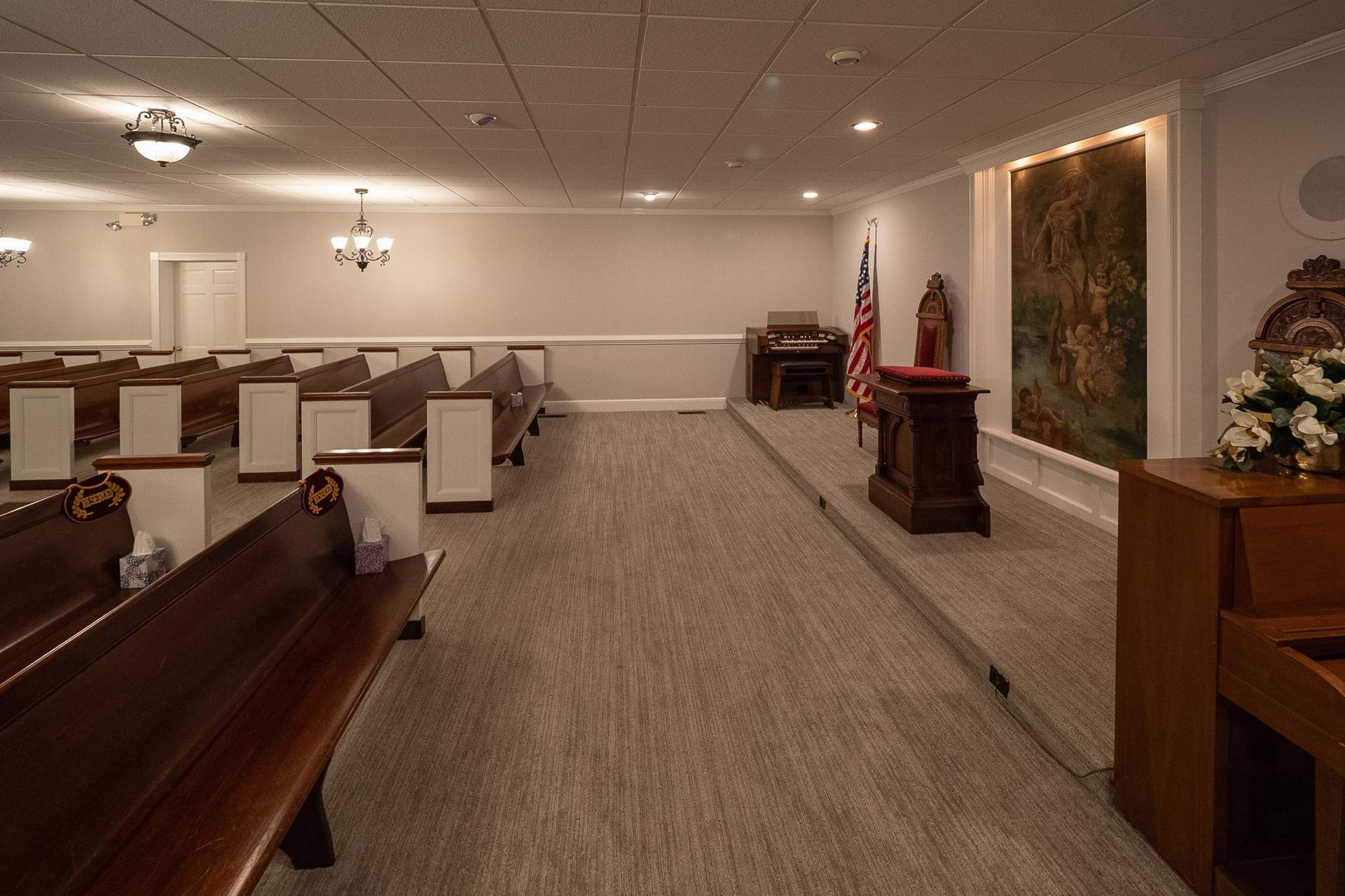 Empty funeral chapel with rows of pews, a casket, and floral arrangements near the front altar.