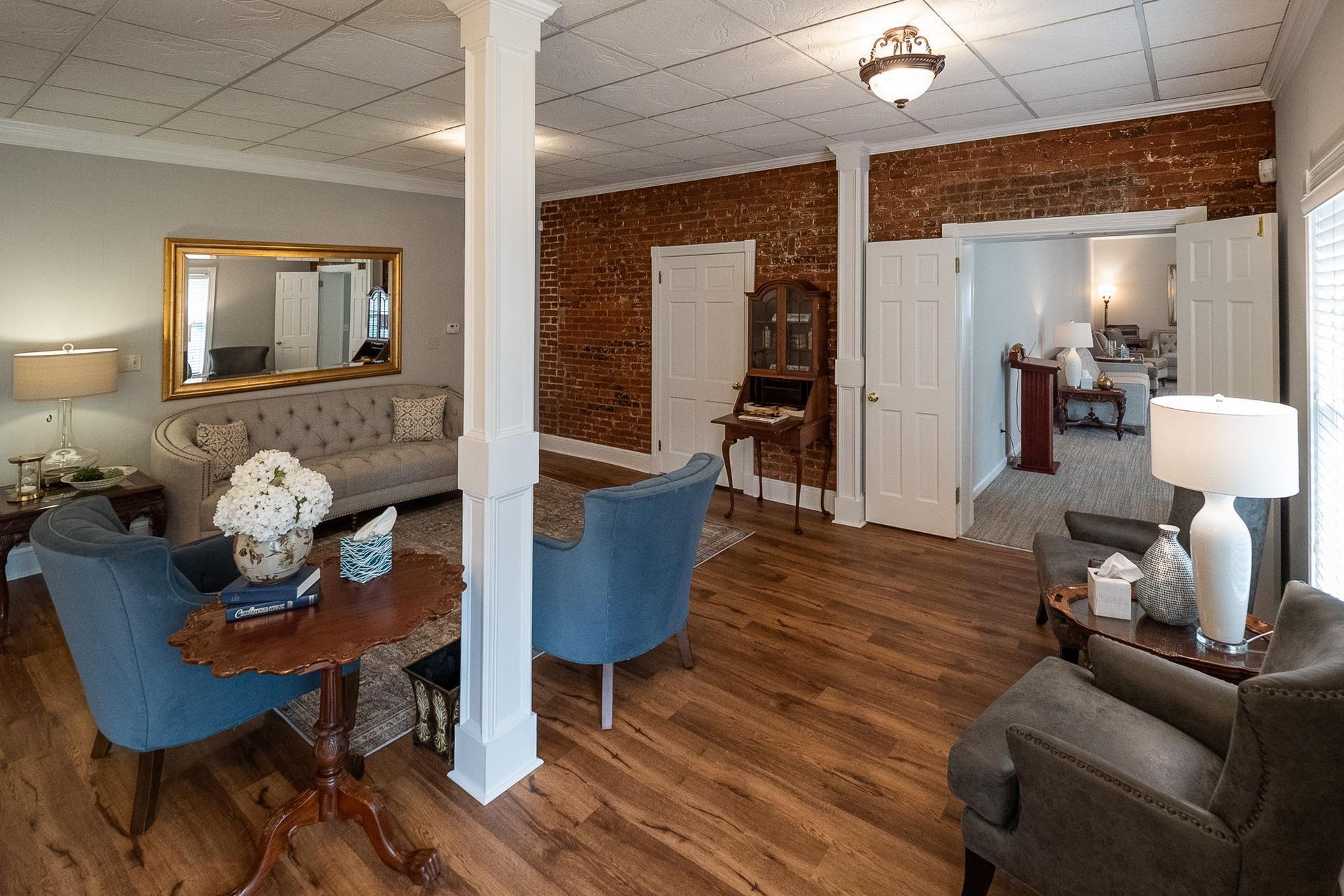 Cozy living and dining area with blue chairs, white columns, wood floors, and a lamp-lit seating nook