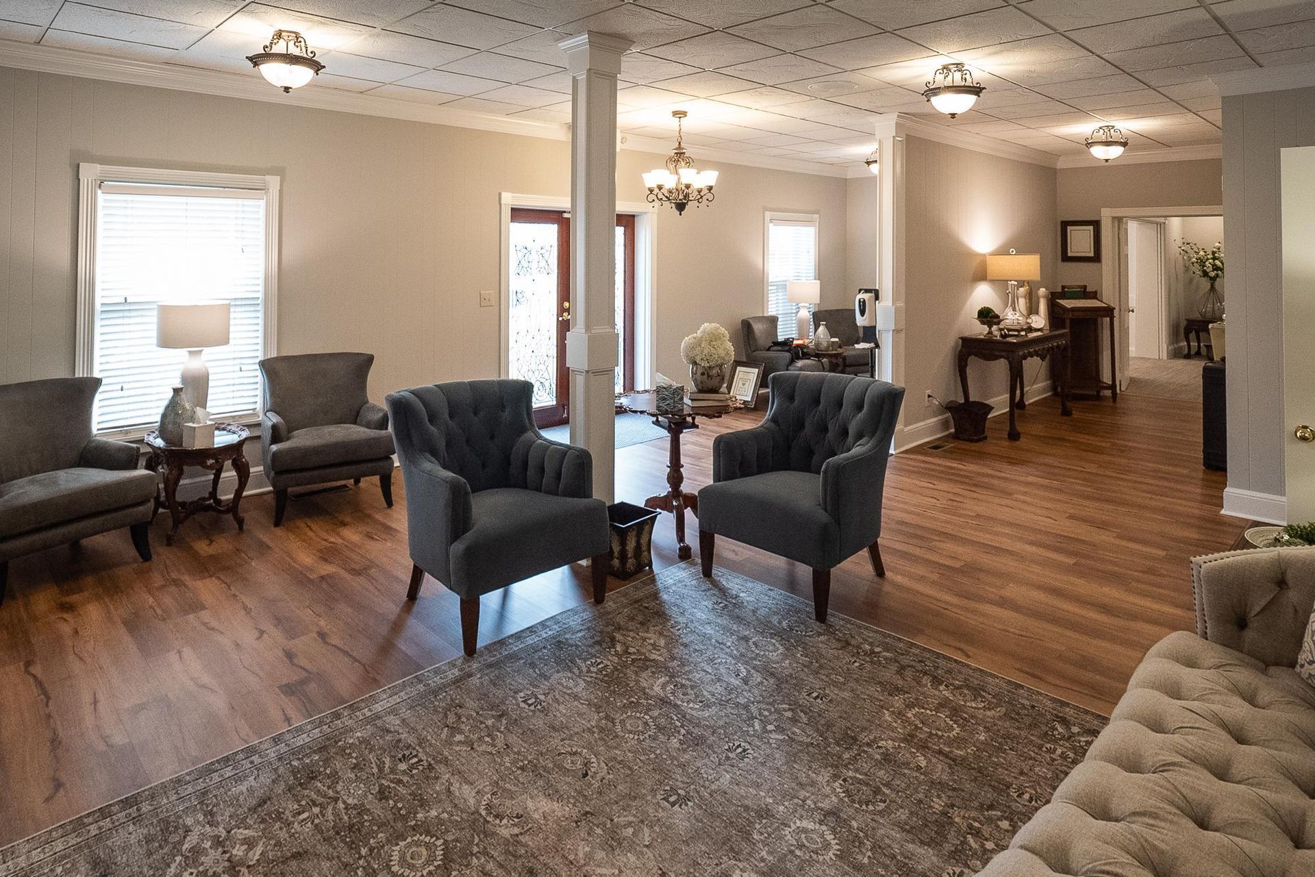Spacious living room with hardwood floors, gray chairs, sofa, rug, and chandelier lighting