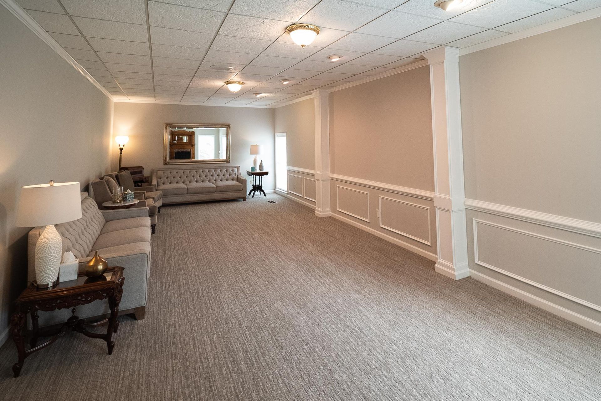 Spacious beige living room with carpet, sofas, and ceiling lights, viewed from the corner