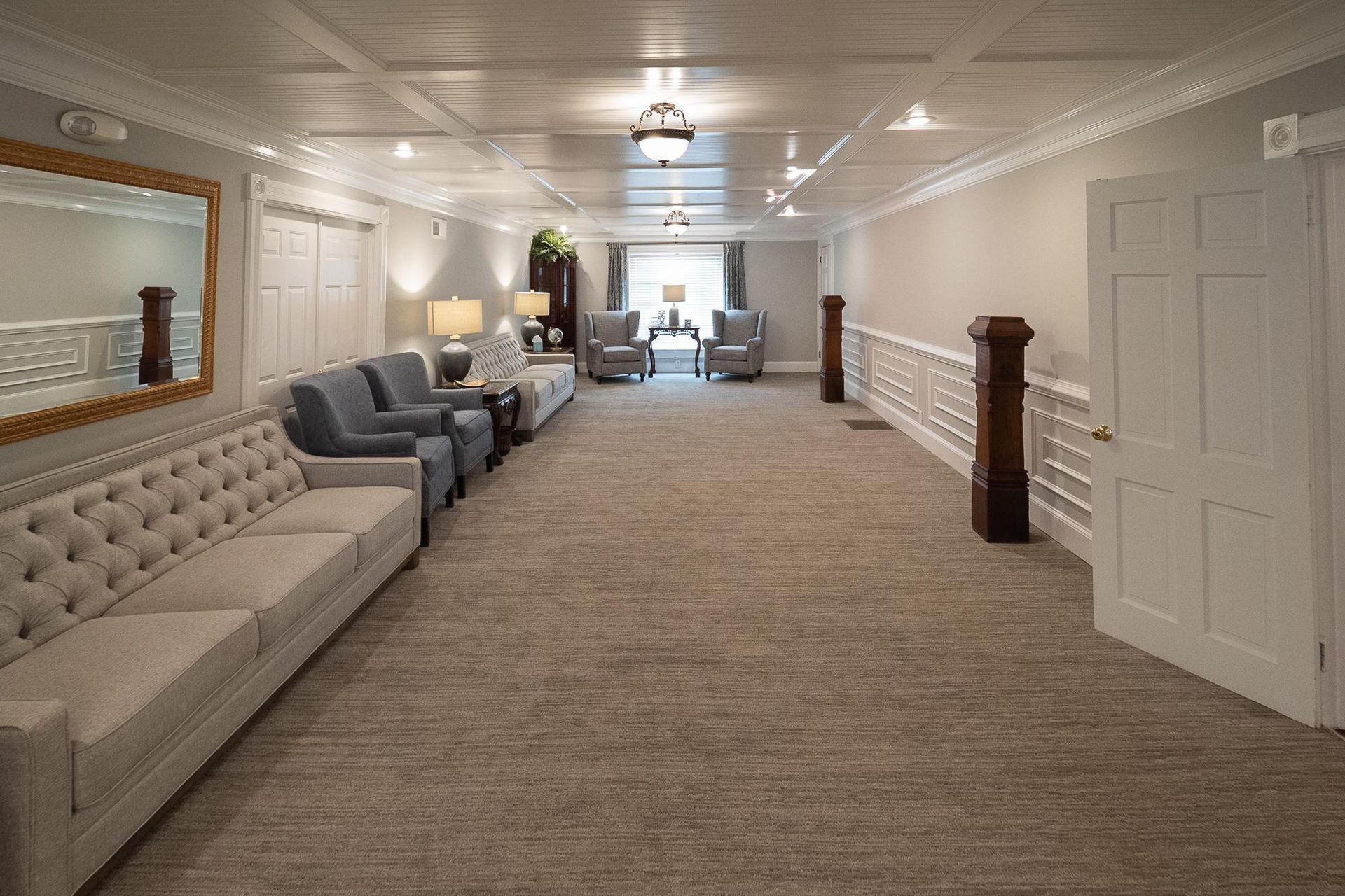 Bright hallway seating area with upholstered couches, lamps, and carpeted floor