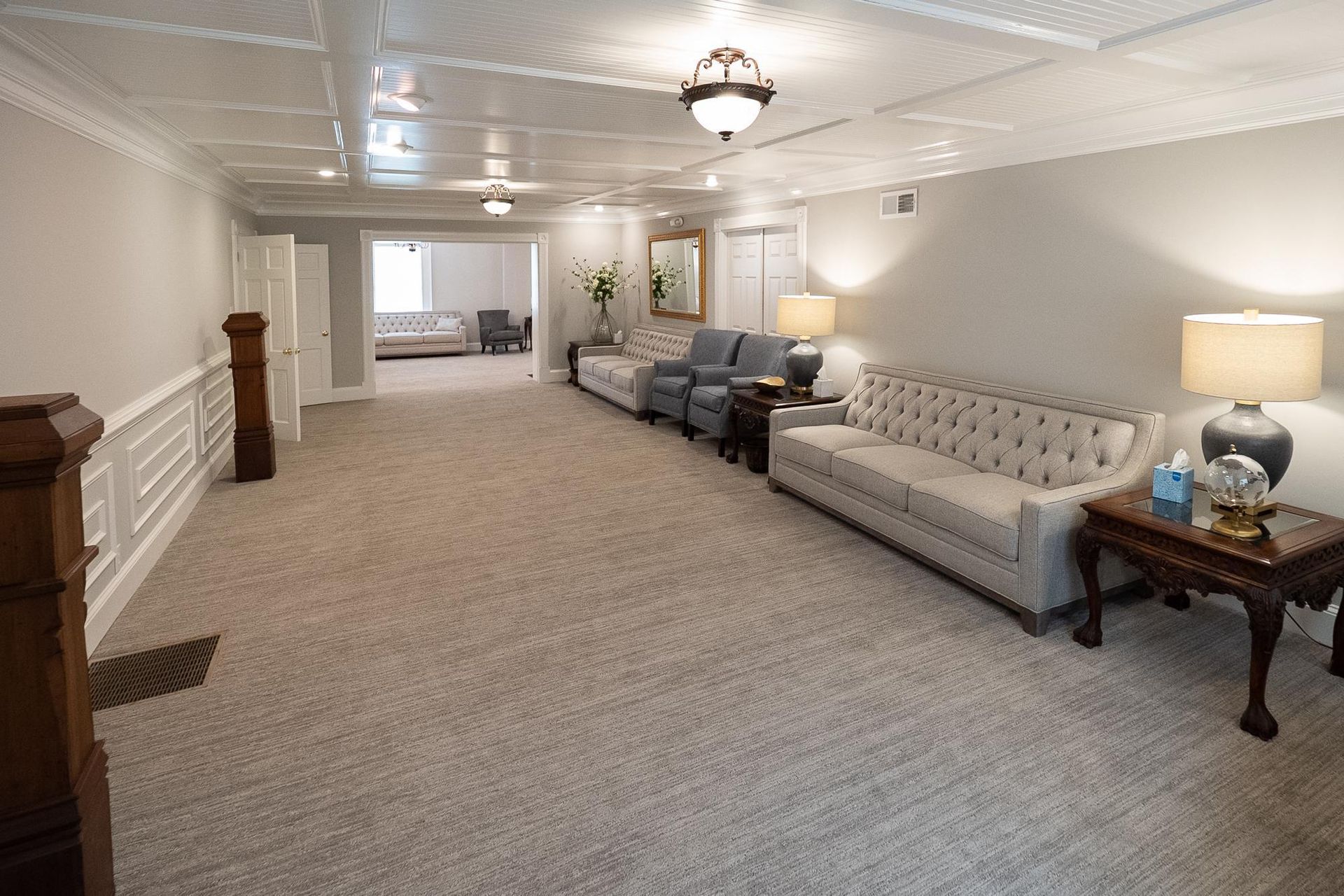 Long carpeted hallway with white walls, ceiling lights, and seating area with sofas and lamps