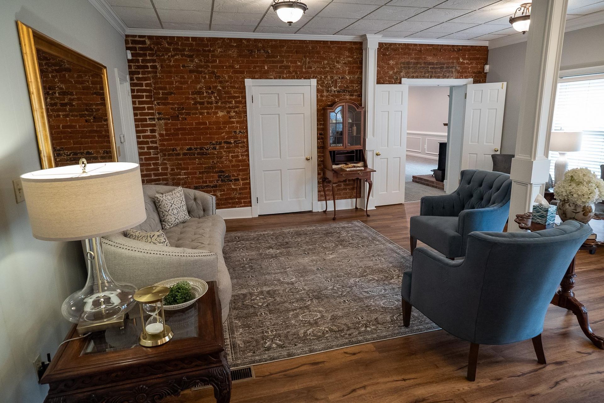 Cozy living room with exposed brick walls, white doors, blue chairs, and a lamp by a side table.