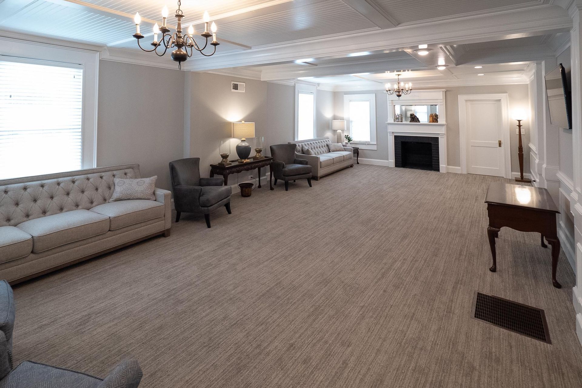 Spacious beige living room with tufted sofas, chandelier, fireplace, and large windows