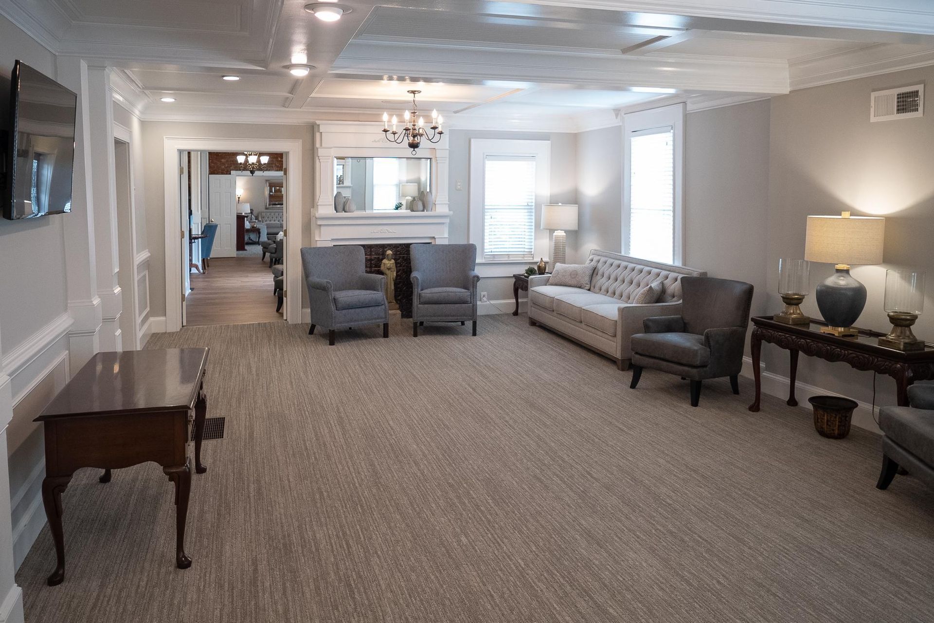 Spacious living room with beige carpet, gray sofa, chairs, and a dining area in the back