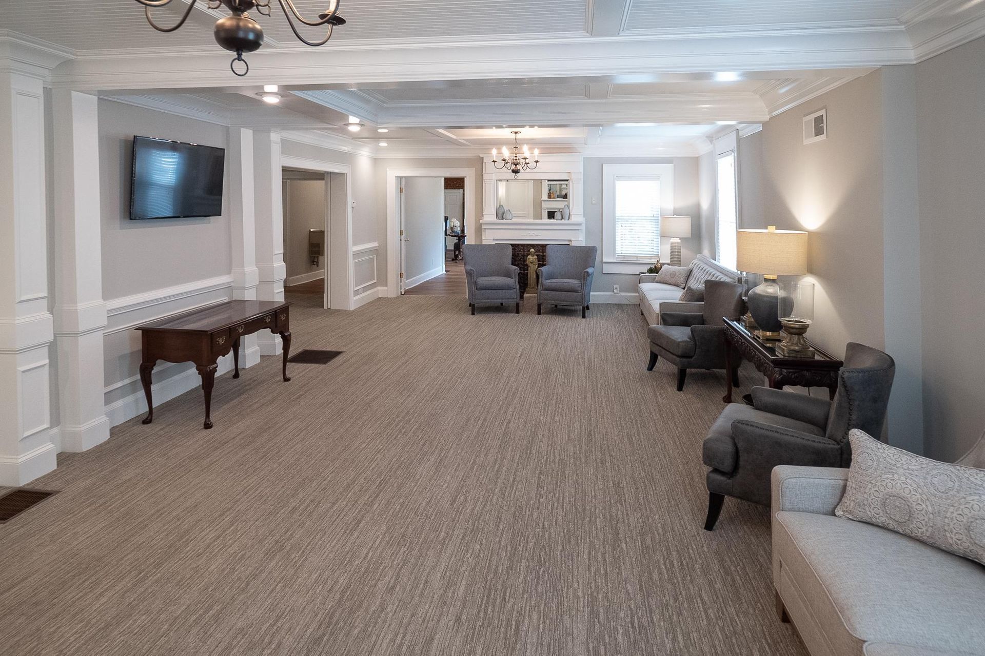 Spacious beige living room with carpet, sofas, lamps, and a wall-mounted TV.