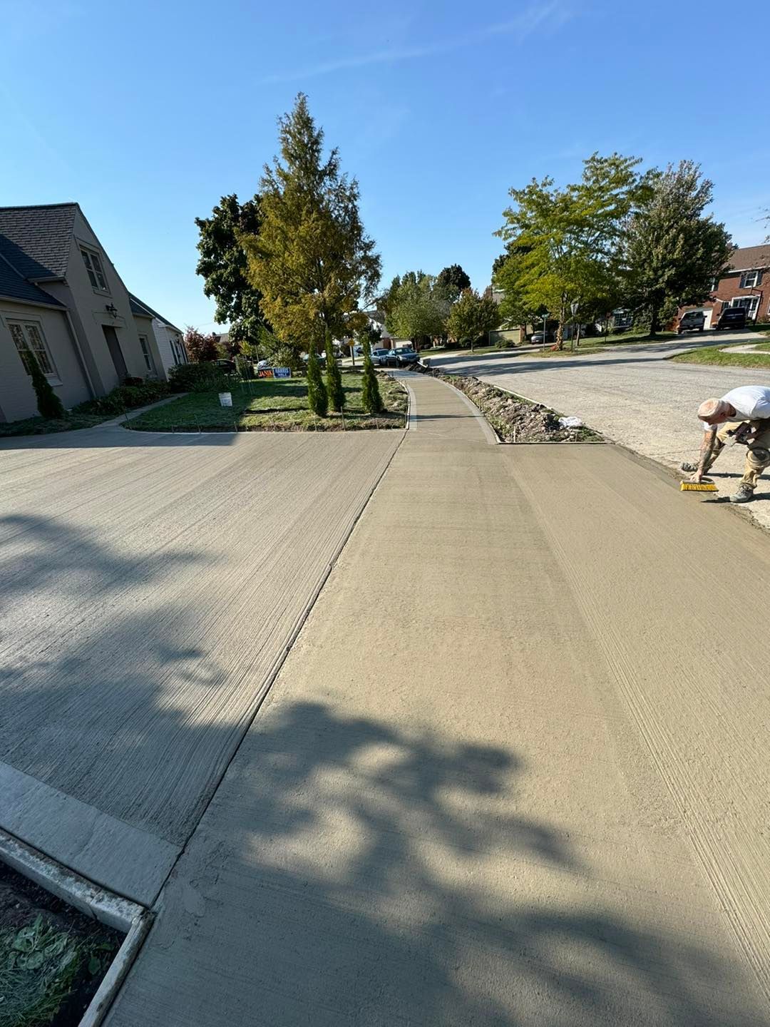 A man is working on a concrete driveway in a residential neighborhood.