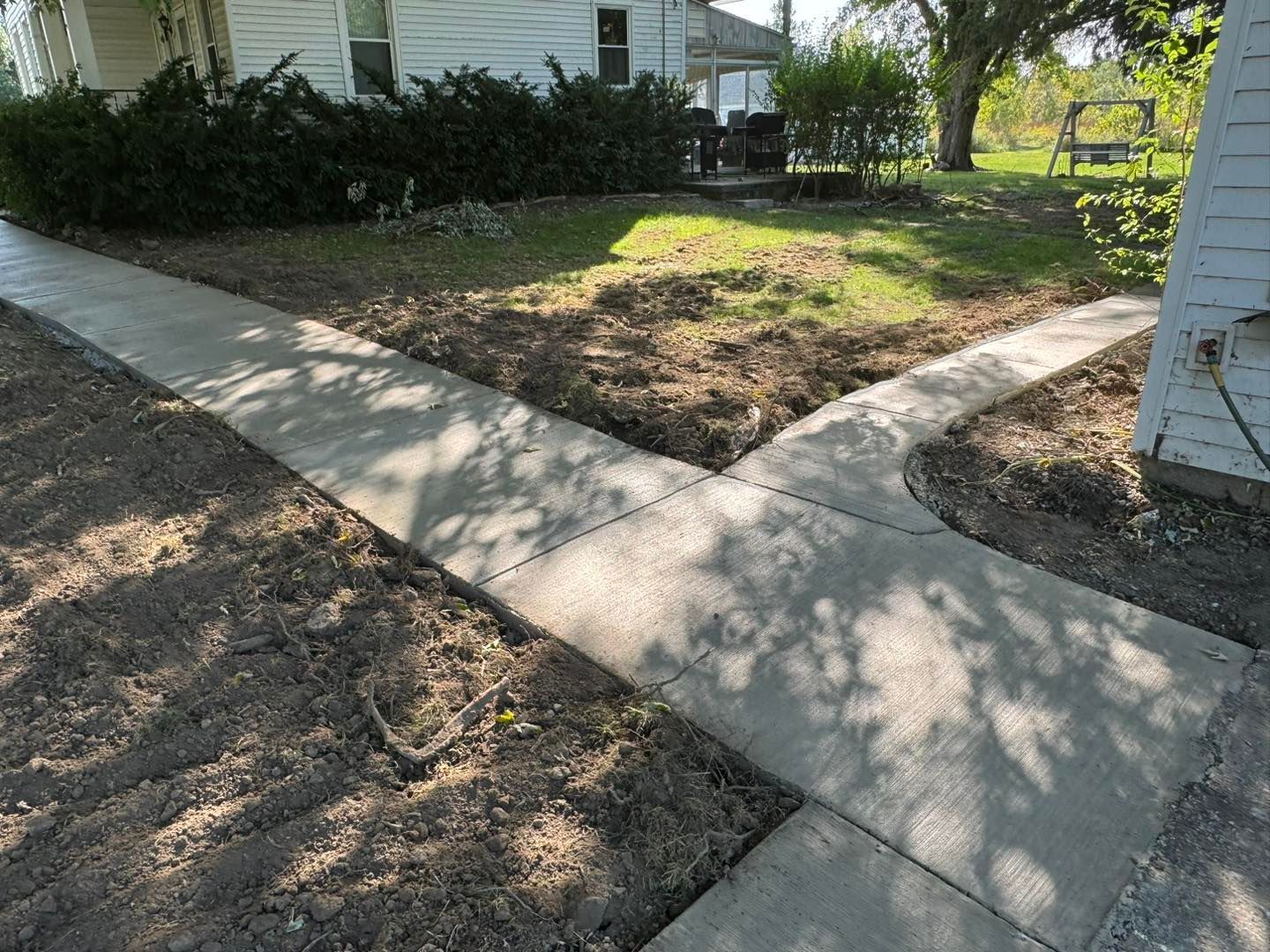A concrete sidewalk leading to a house with a bench in the background.