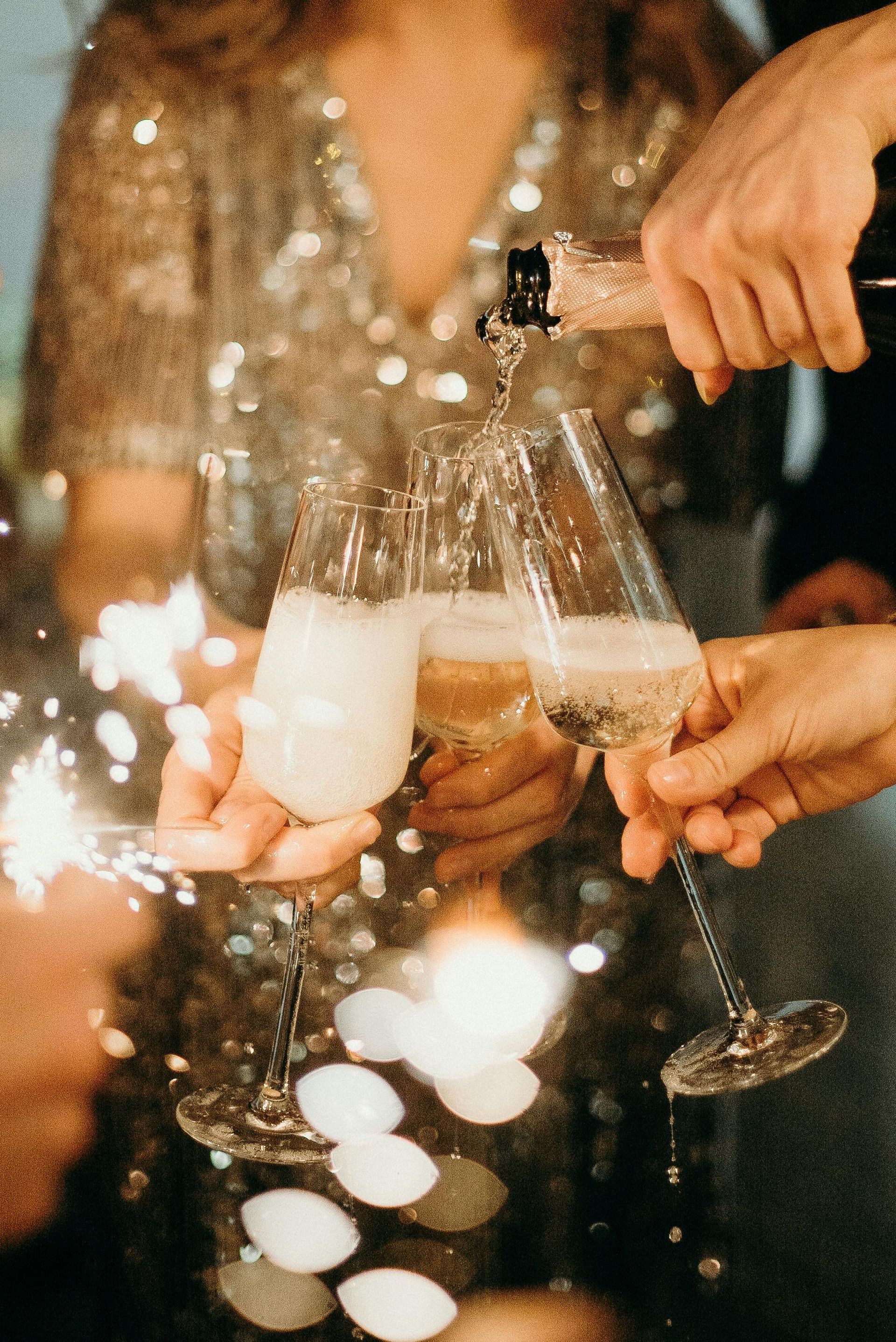 Champagne being poured into three flutes as a sparkler is lit.
