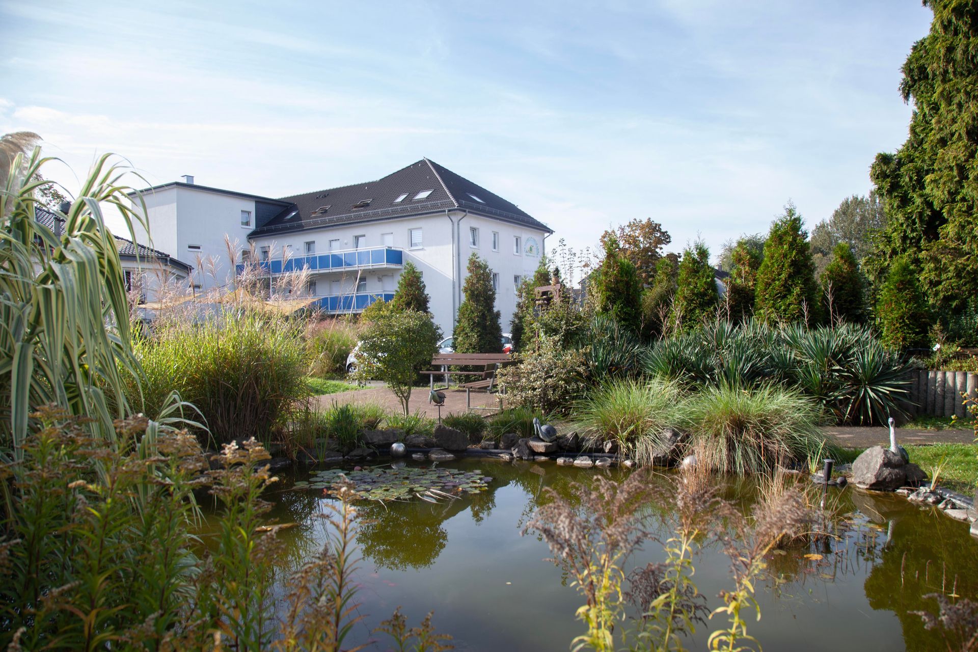 Objektfoto, weißes Wohnhaus an einem Park mit Gartenteich