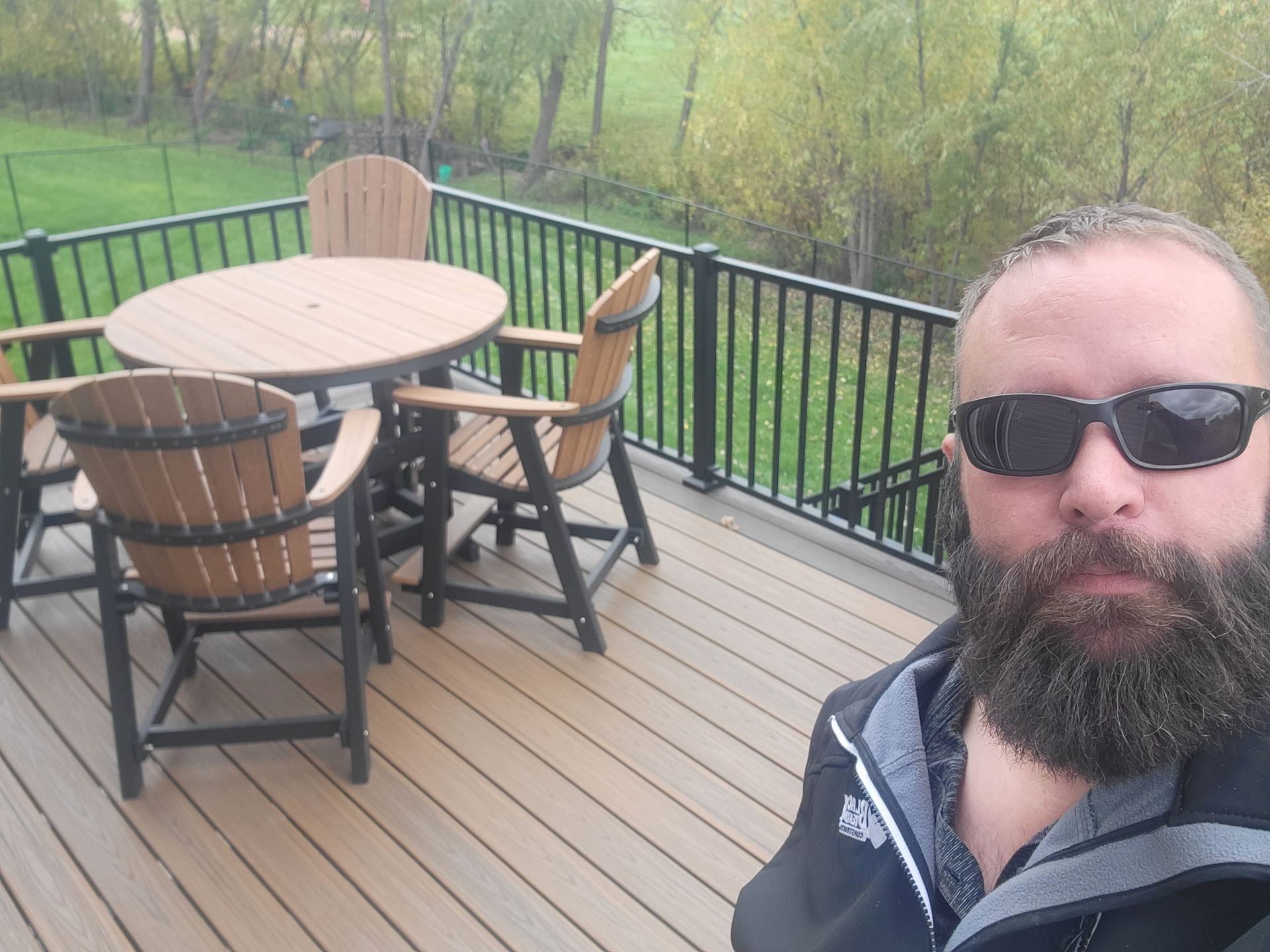 A man with a beard is standing on a deck with a table and chairs.