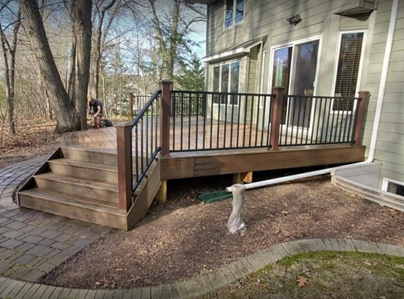 A wooden deck with stairs and a metal railing in front of a house.
