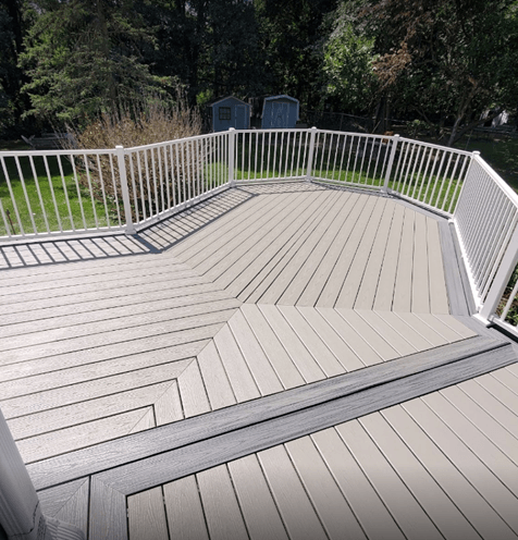 A gray deck with a white railing and trees in the background