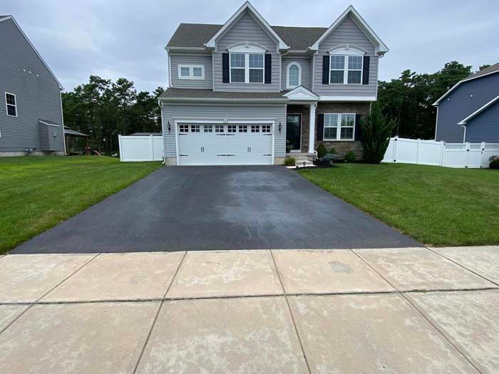 Two-story gray house with a black asphalt driveway and green lawn.