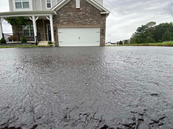Flooded driveway in front of a house with a white garage door, water reflecting the overcast sky.