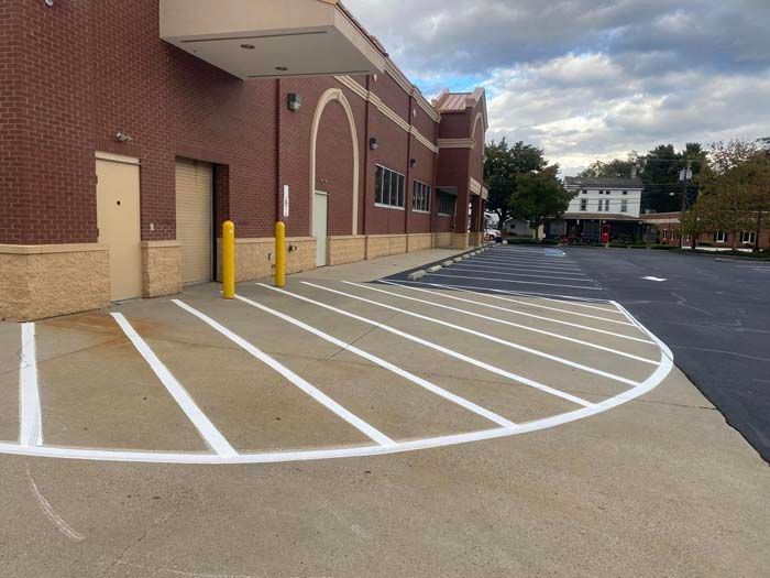 Exterior of a brick building with striped parking/loading area; yellow poles, paved area, and a building entrance.