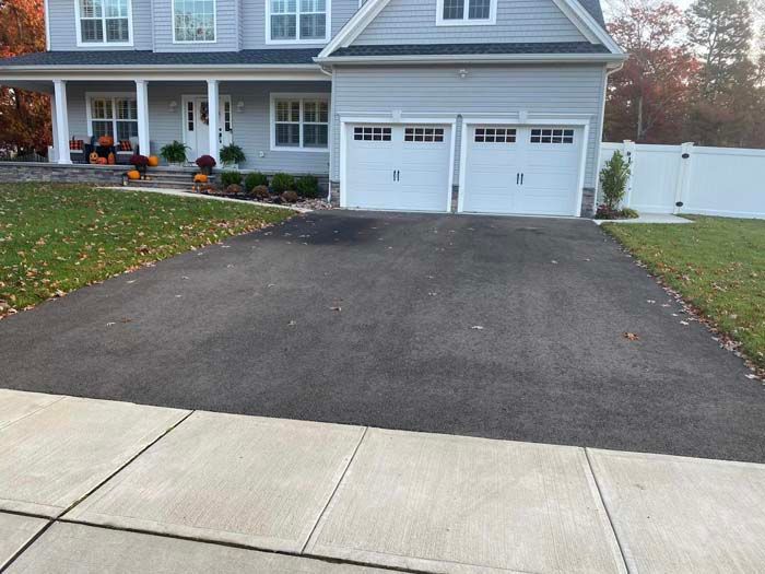 Asphalt driveway leading to a two-car garage of a two-story gray house with a white front porch.