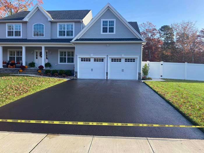 Newly paved black asphalt driveway in front of a light gray house with a two-car garage.