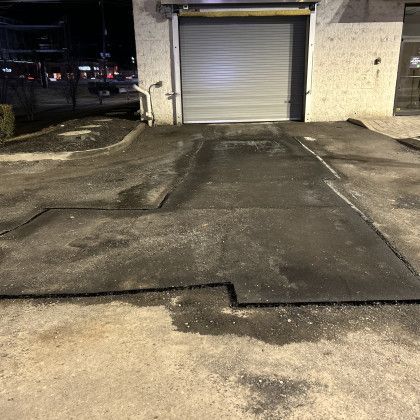 Asphalt driveway with a raised section leading to a closed garage door. Streetlights illuminate the scene at night.