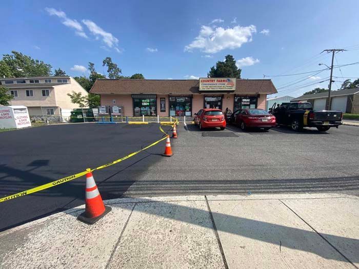 Newly paved asphalt parking lot outside a small business with parked cars and safety cones.