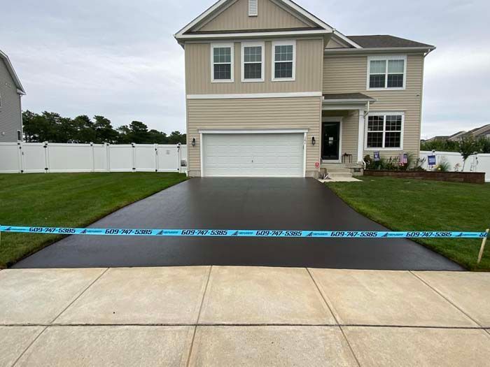 Newly paved black asphalt driveway in front of a tan two-story house with green lawn.