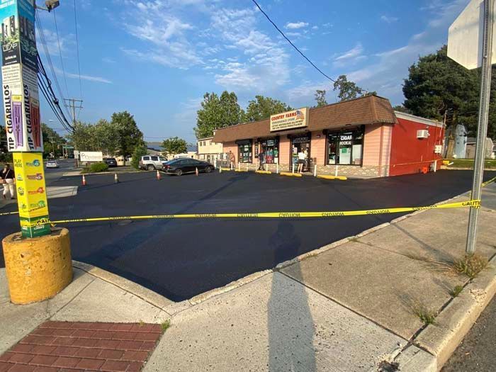 Newly paved parking lot in front of a small brick store; caution tape, utility pole in foreground.