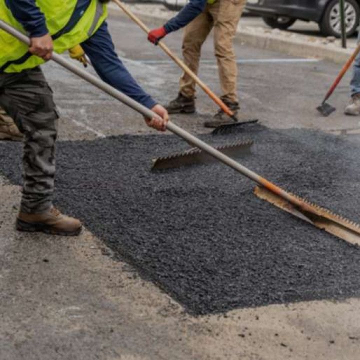Road workers paving asphalt with rakes. Patch of black asphalt, surrounded by gray pavement.