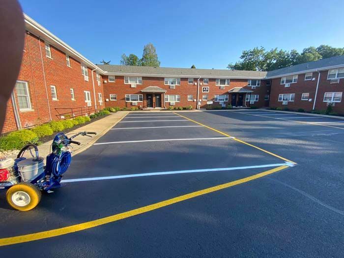 Freshly painted parking lot with white and yellow lines, in front of a red brick building. A striping machine is visible.