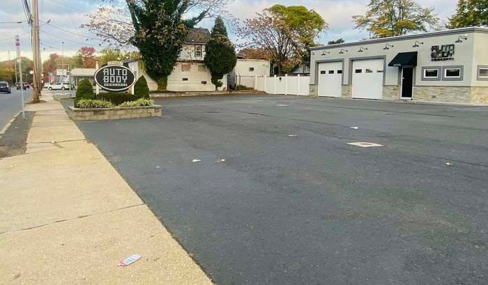 Asphalt parking lot next to a sidewalk and a building with garage doors.