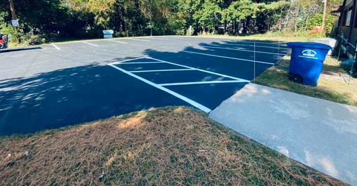 Newly paved parking lot with white painted lines and a blue trash bin.
