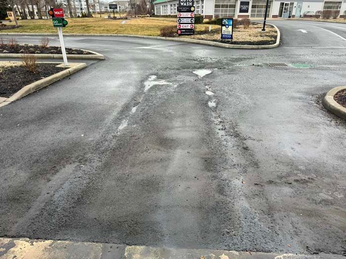 Asphalt driveway with tire tracks, near a traffic light and businesses.