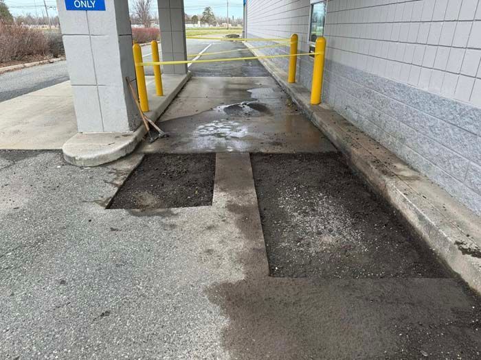 Drive-thru lane with sections of asphalt removed, exposing gravel. Yellow barriers and support columns are present.