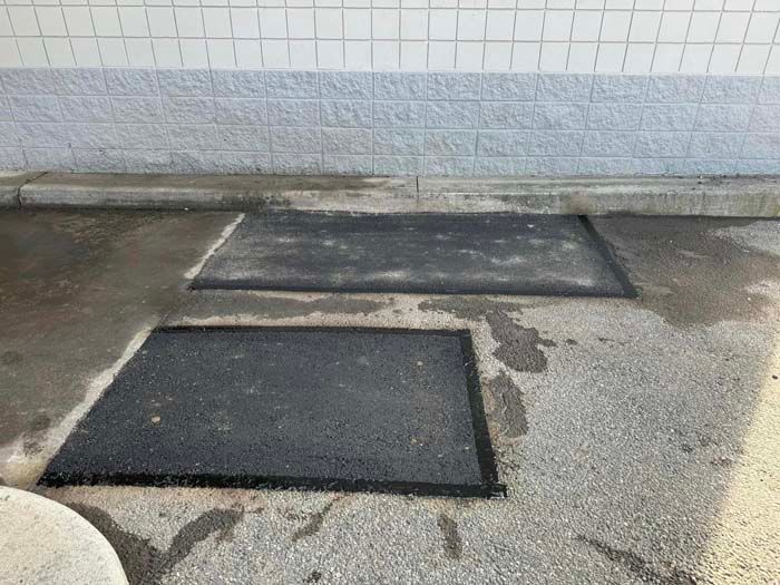 Asphalt patches in a parking area against a white-tiled wall.