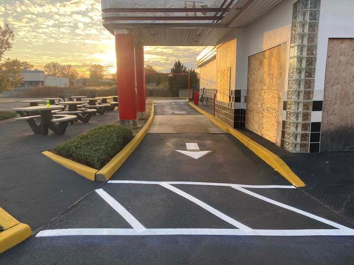 Drive-thru lane with an arrow, a red pillar, and picnic tables in front of a fast-food restaurant.