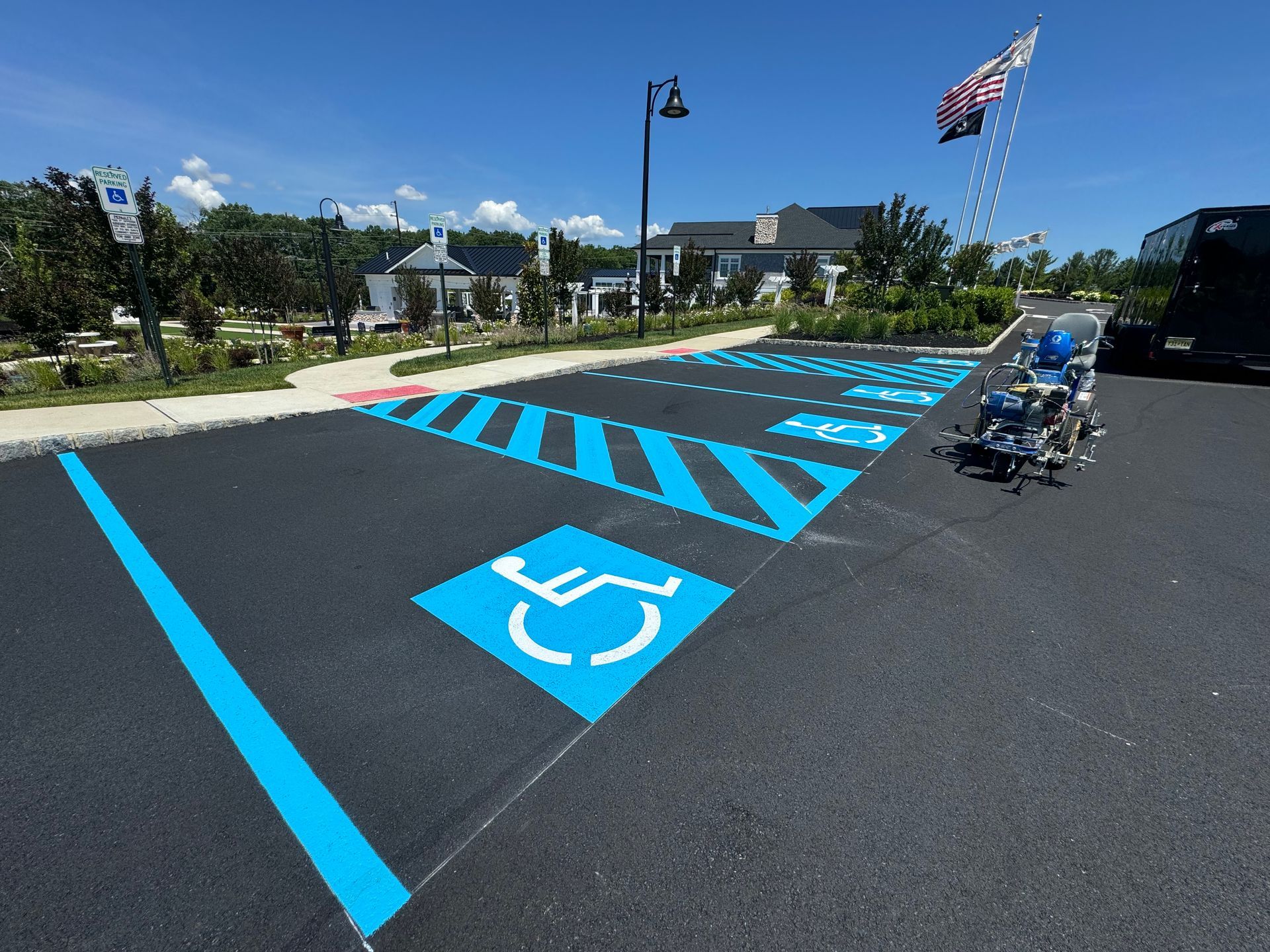 Handicap parking spaces marked in blue on asphalt, with a building and flag in the background.